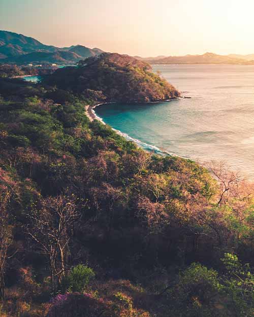 Panoramic view of Drake Bay in Costa Rica, with green hills and calm sea at sunset.